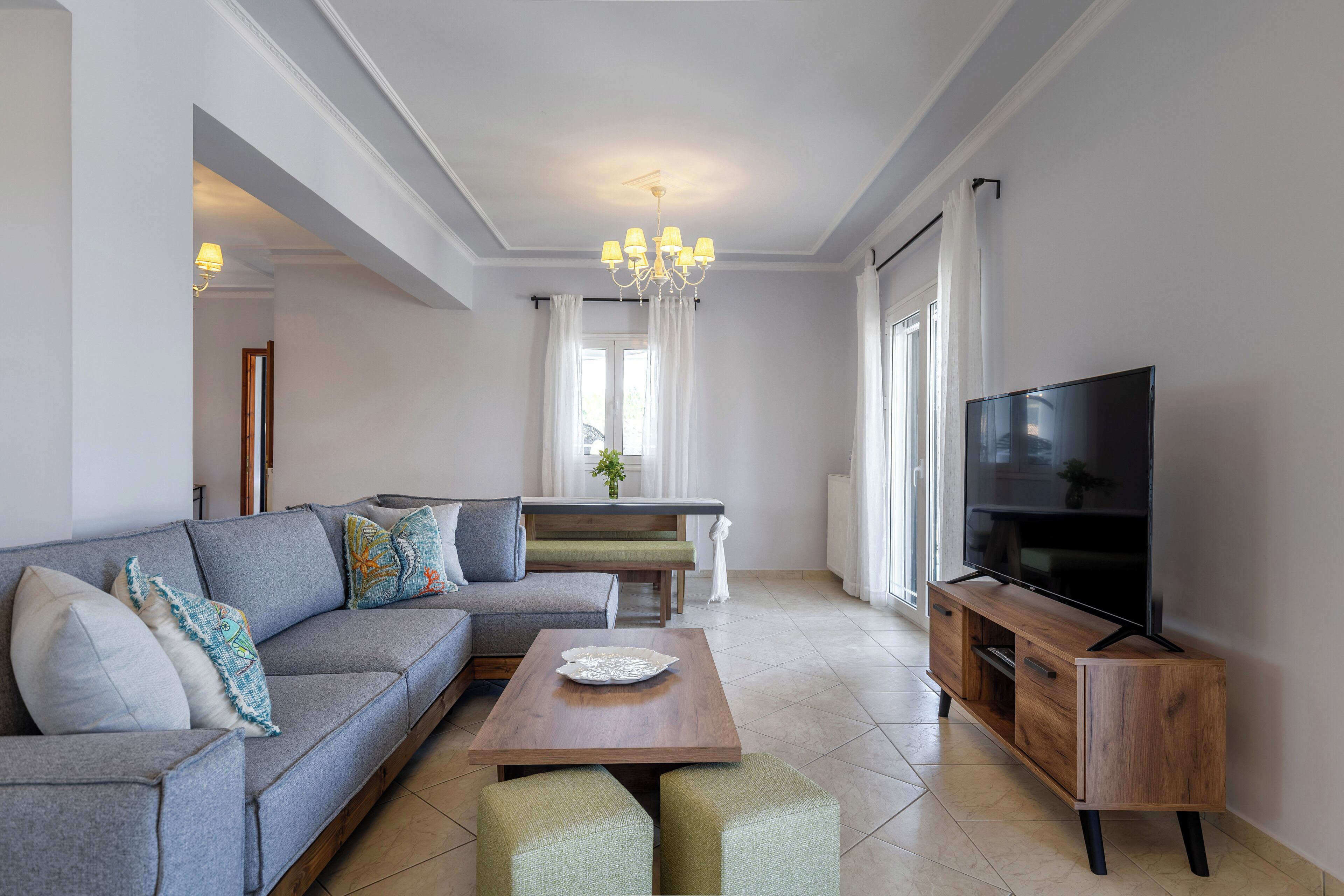 Una sala de estar moderna con un sofá modular, una mesa de centro de madera, un mueble para televisor y un área de comedor con un banco y cortinas.