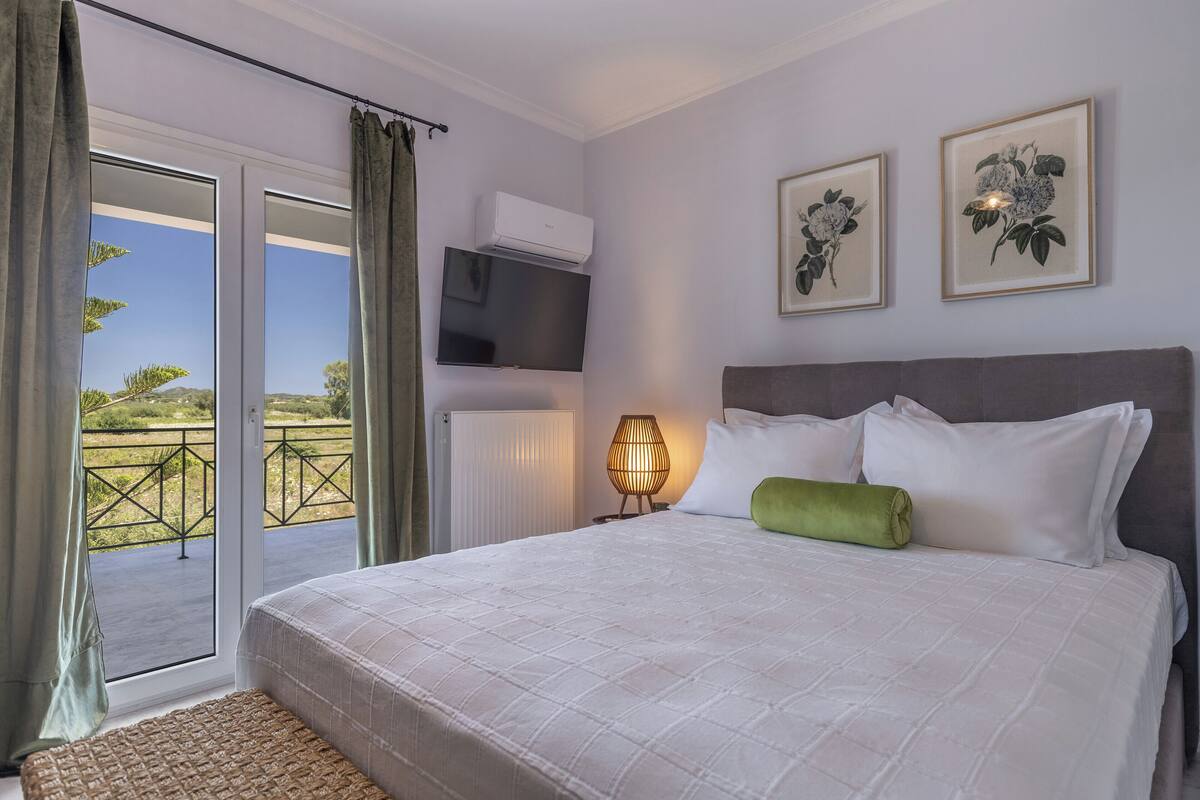 Une chambre avec un grand lit, une télévision, une lampe et une porte-fenêtre coulissante donnant sur un balcon.