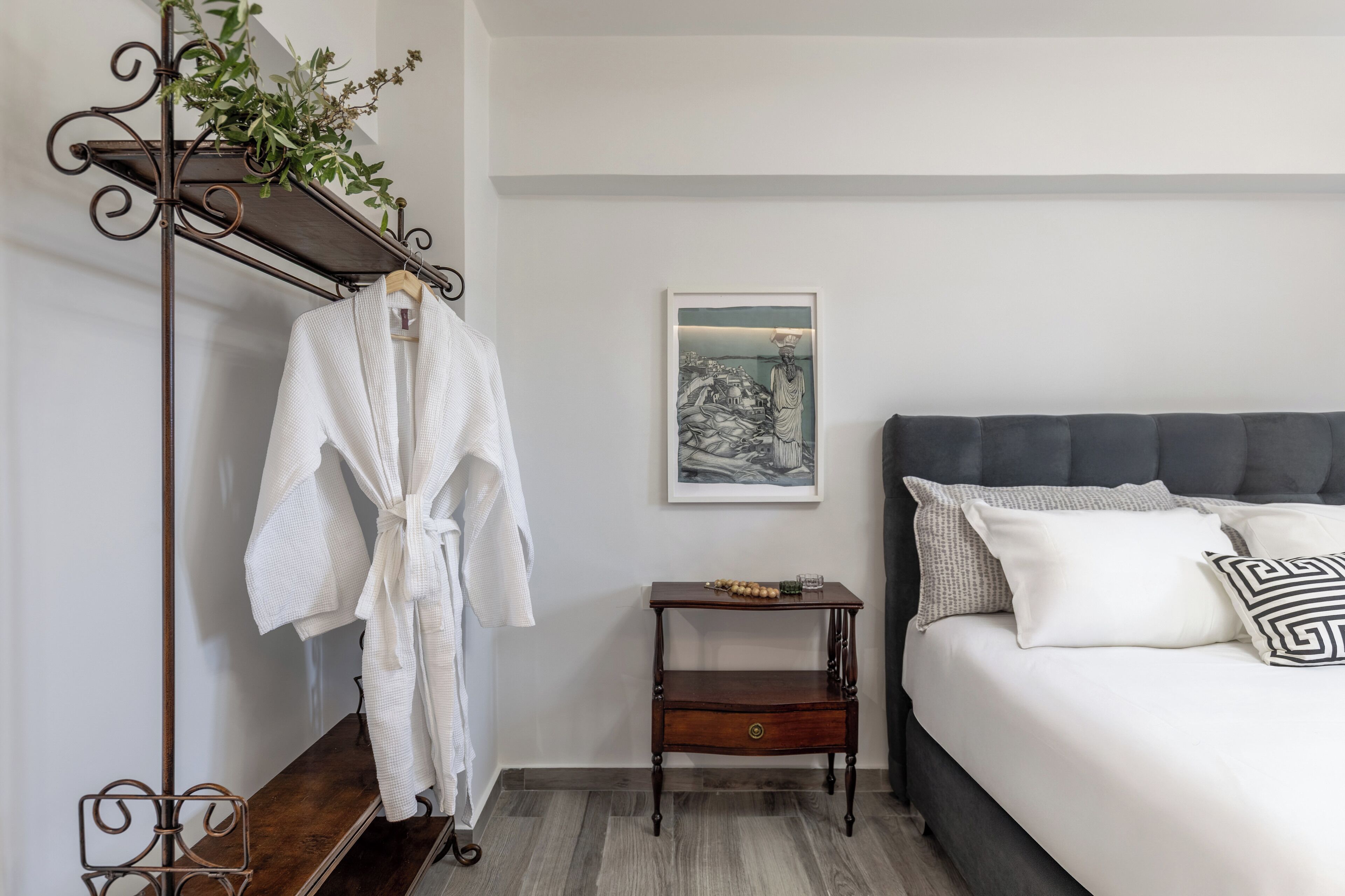 Een netjes opgemaakt slaapkamer met een bed, een nachtkastje, een kledingrek en een ingelijste foto aan de muur.