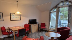 A compact living space with a dining area, a sofa, a TV, and a window with curtains. - Classic apartment with 1 bedroom and balcony on the top floor (Ostseebad Binz)