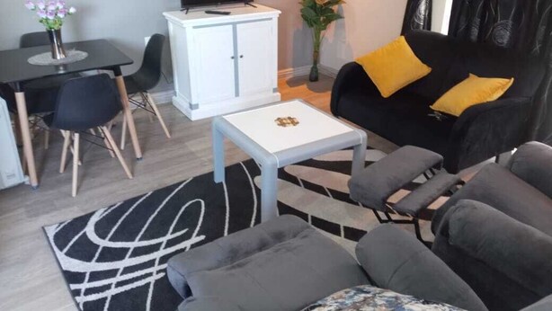 Un salon moderne avec un canapé noir, une table basse blanche et un coin repas comprenant une table et des chaises noires.