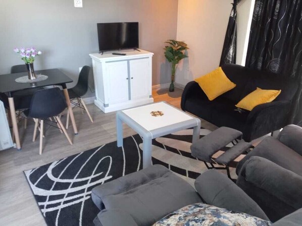 A modern living room with a black sofa, a white coffee table, and a dining area with a black table and chairs.