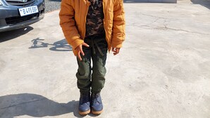 Un enfant se tient sur un parking, avec une voiture et un bâtiment en arrière-plan.