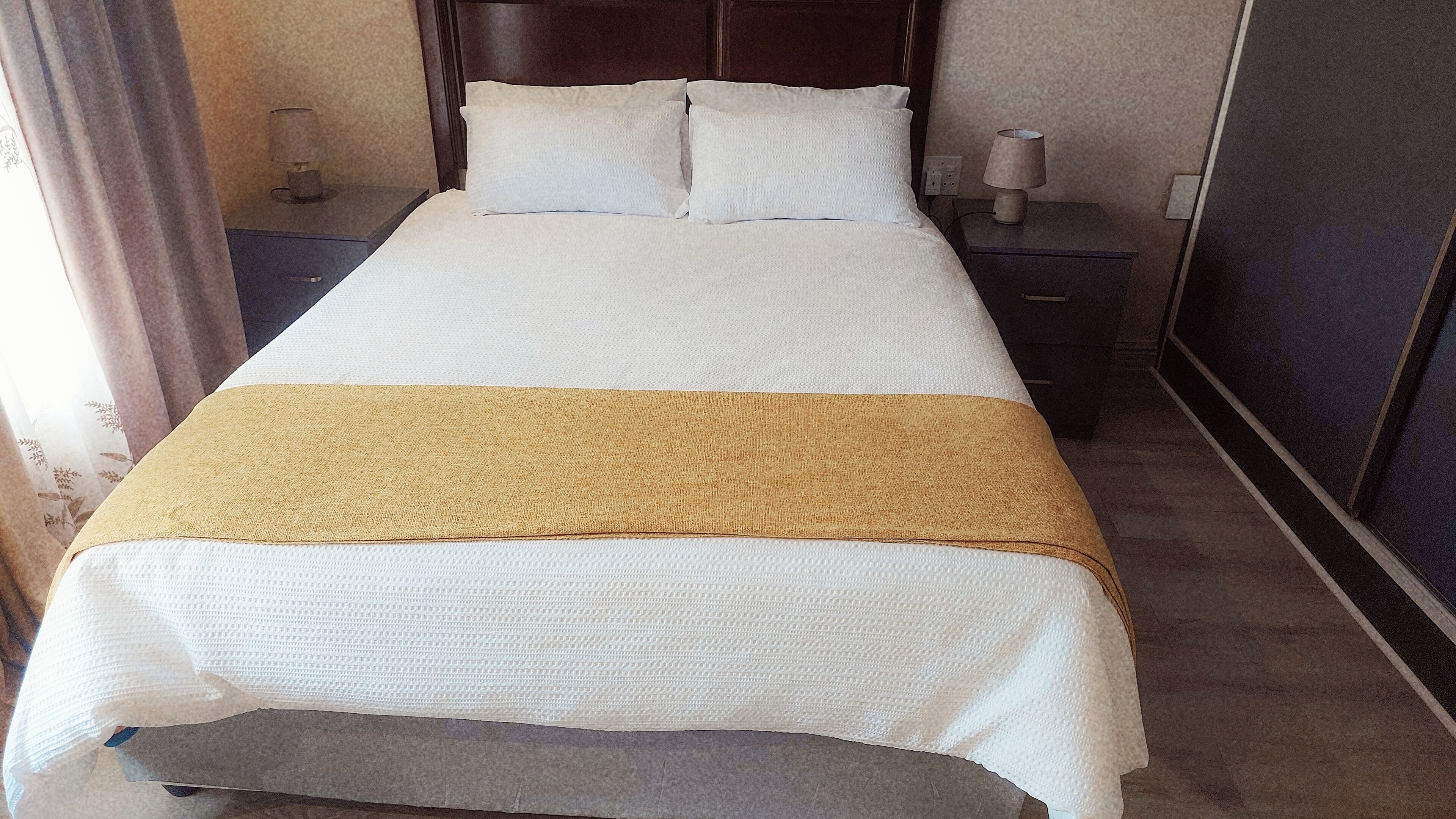A neatly made bed with a white and beige bedspread, two white pillows, and a wooden headboard.