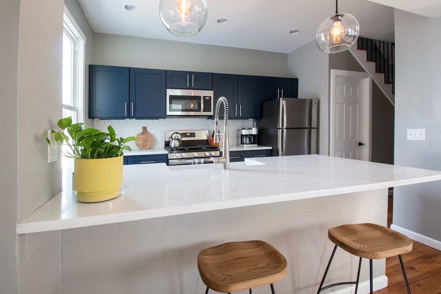 Una cocina moderna con armarios azul oscuro, electrodomésticos de acero inoxidable, una isla blanca con taburetes e iluminación colgante.