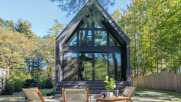 A modern house with large windows, a patio with two chairs and a table, and a wooden fence. - Cozy Cabin On The Esopus Creek in Saugerties, New York (Saugerties)
