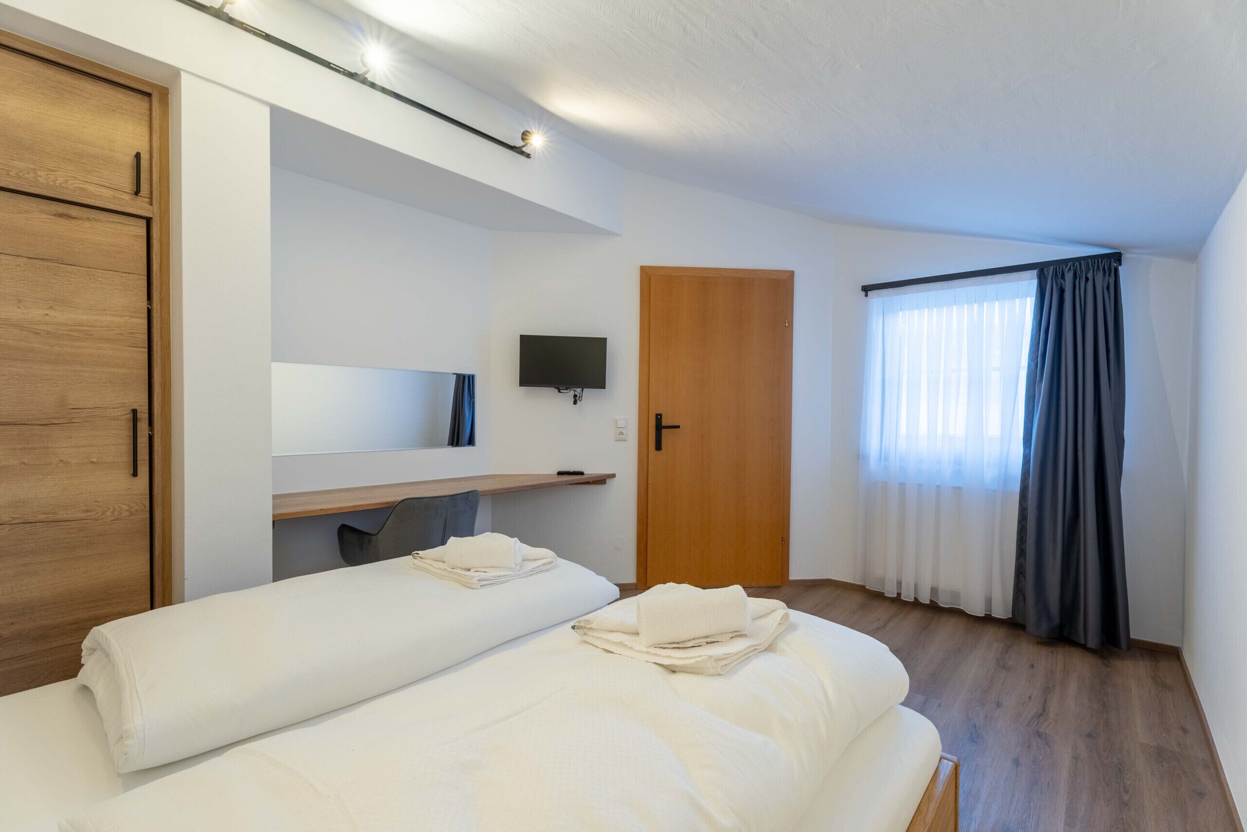 Una habitación de hotel con cama, armario de madera, televisor, escritorio y ventana con cortinas.