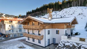 A modern chalet with a wooden balcony, a ski lift in the background, and a snowy hillside. - Alpenglück Apartments - 3 (Saalbach)