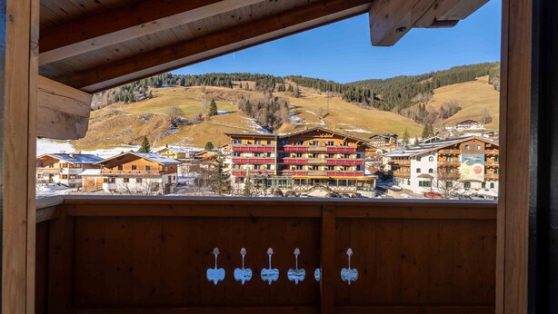 A wooden balcony with a view of a mountain village, featuring multi-story buildings with balconies and a clear sky. - Alpenglück Apartments - 3 (Saalbach)