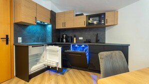 A compact kitchen with wooden cabinets, a microwave, a dishwasher, and a coffee maker. - Alpenglück Apartments - 3 (Saalbach)