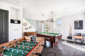 A room with a foosball table, pool table, and a staircase. - Gîte Les Hervelines with Private Pool, Garden & Wi-Fi in Pleudihen sur Rance (PLEUDIHEN SUR RANCE)