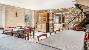 Un espace repas avec des tables et des chaises en bois, un mur en pierre et un escalier en bois.
