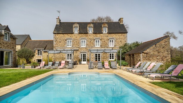 Un bâtiment en pierre doté d’une piscine et de chaises longues.