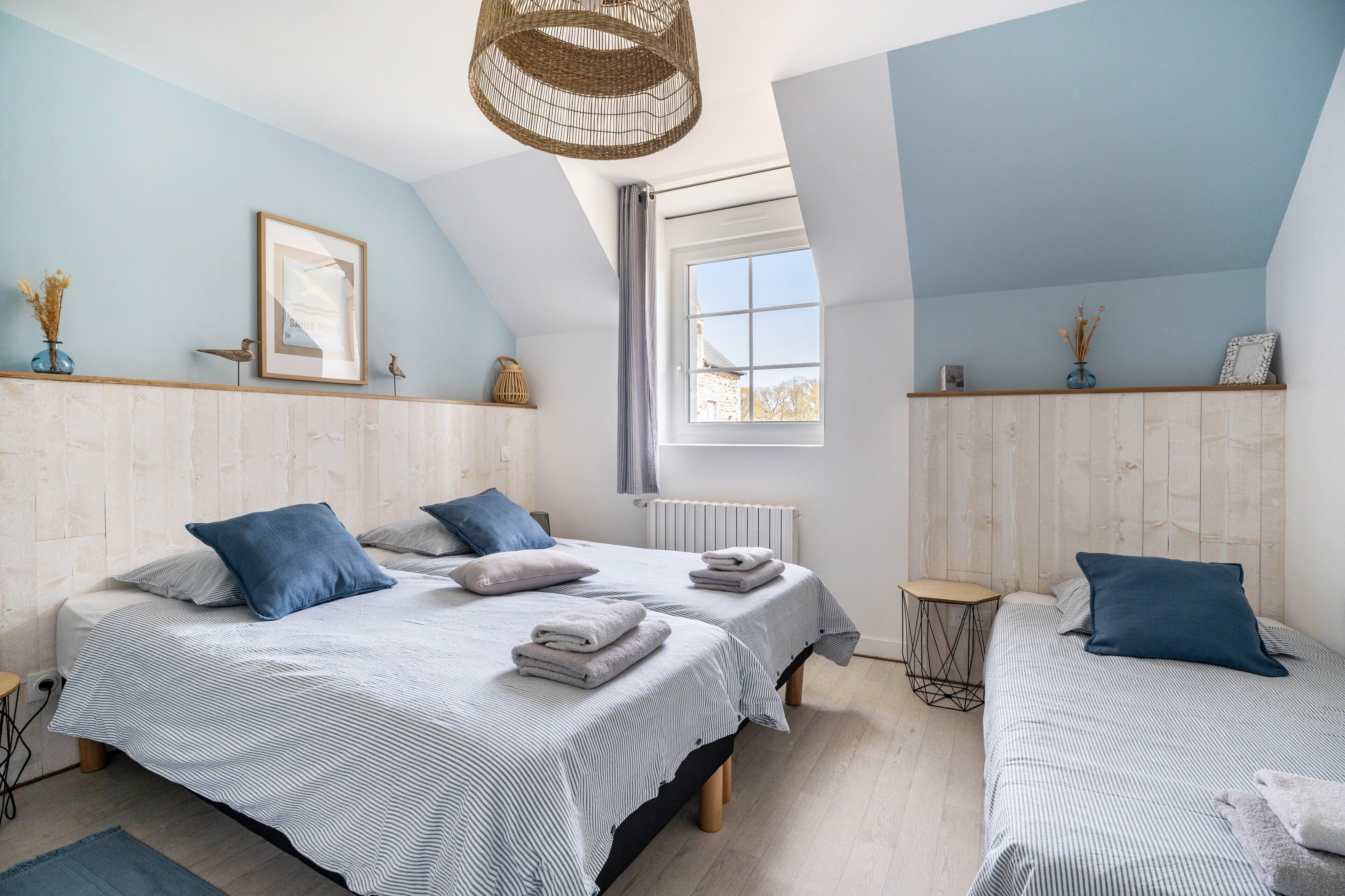 A bedroom with two beds, a window, a radiator, and a wooden headboard.