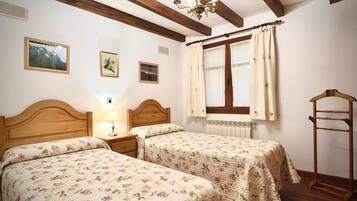 Een slaapkamer met twee bedden, houten hoofdeinden, een raam met gordijnen, een radiator en een houten ladder.