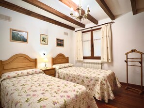 Un dormitorio con dos camas, cabeceros de madera, una ventana con cortinas, un radiador y una escalera de madera.