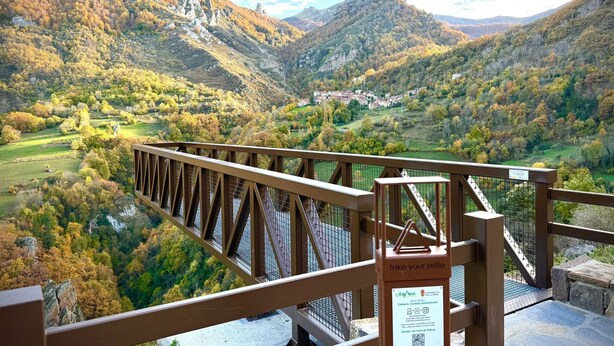 A scenic view from a bridge overlooking a valley with autumn foliage, a sign encouraging visitors to take selfies, and a QR code for more information.
