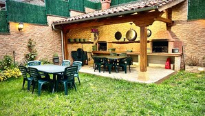 An outdoor patio with a brick barbecue area, a table with chairs, and a pergola structure.