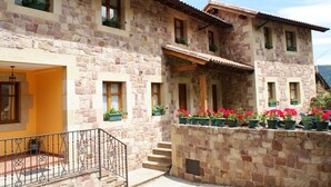 A stone building with multiple windows, a balcony with a railing, and potted plants on the exterior wall.