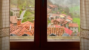A view through a wooden-framed window with a view of a village with red-roofed buildings and a mountain in the background.