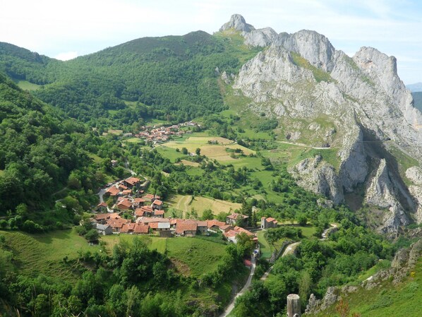 Un pueblo ubicado en un valle con campos en terrazas y una montaña destacada al fondo.