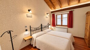 A bedroom with two beds, a wooden ceiling, a radiator, and a window with red curtains.