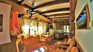 A cozy living room with wooden beams, a dining area, and a kitchen.