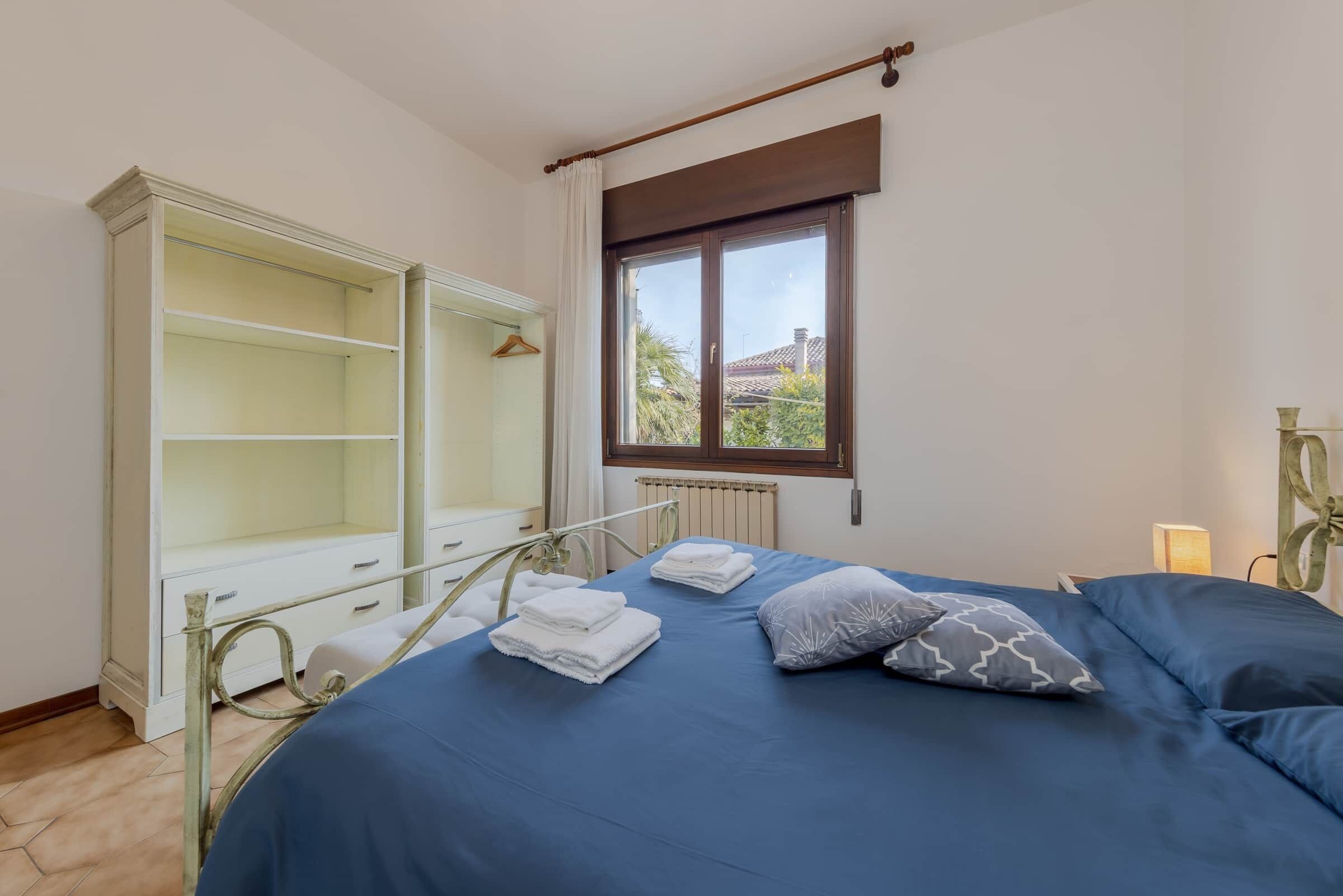 A bedroom with a bed, a wardrobe, and a window with a view of the outside.
