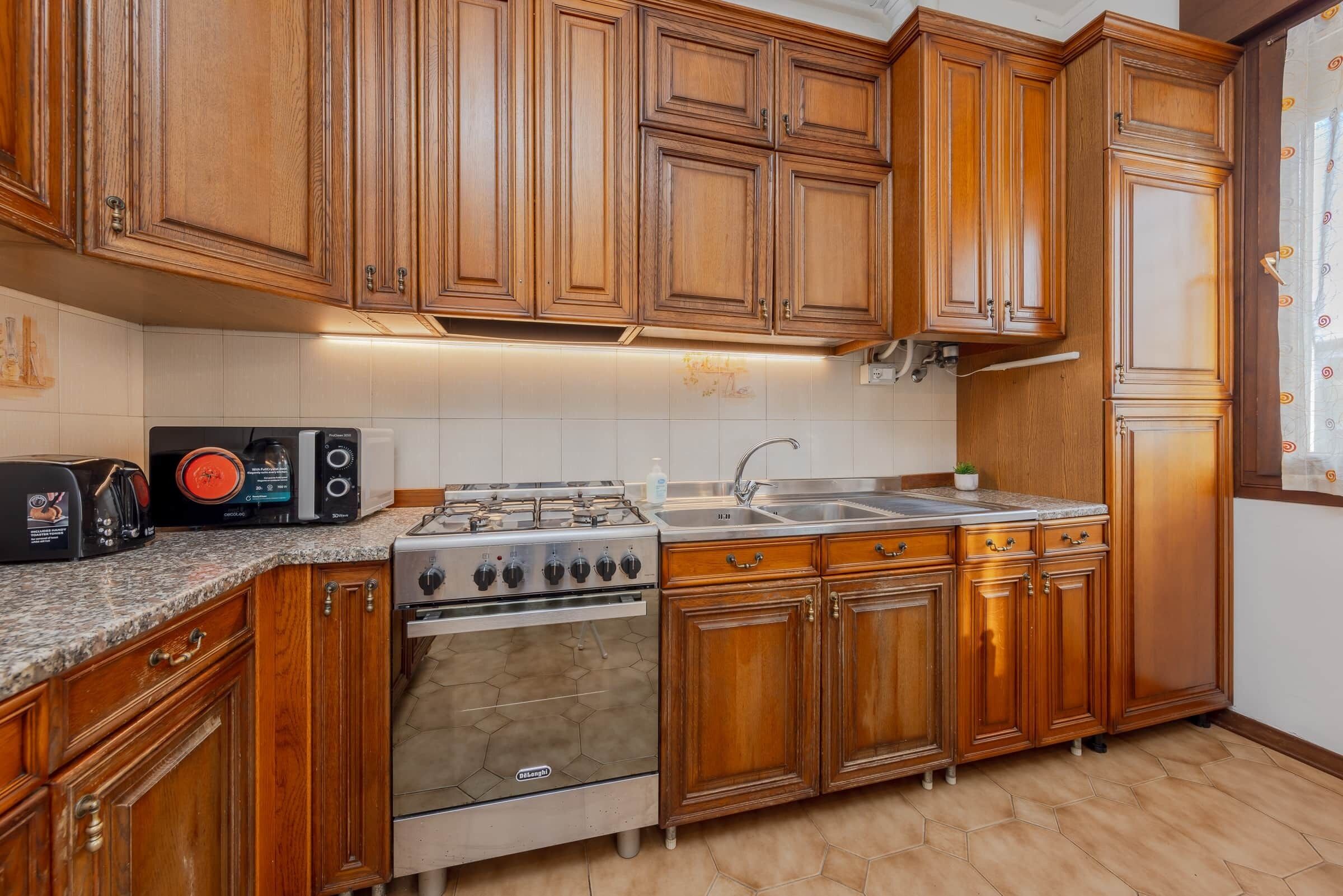 Cucina con mobili in legno, piano cottura a gas, forno a microonde e lavandino.