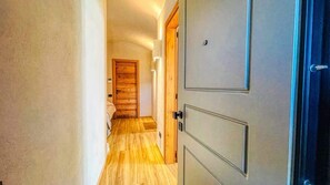 Un corridoio con pavimento in legno, una porta di legno e un interruttore a muro.