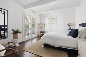 Une chambre à coucher avec un grand lit, une table de chevet, une chaise, une fenêtre avec des stores et une plante.