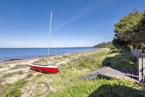A red boat on a sandy beach with a wooden structure and a tree line in the background. - illiac in Somers - absolute beachfront. (Somers)