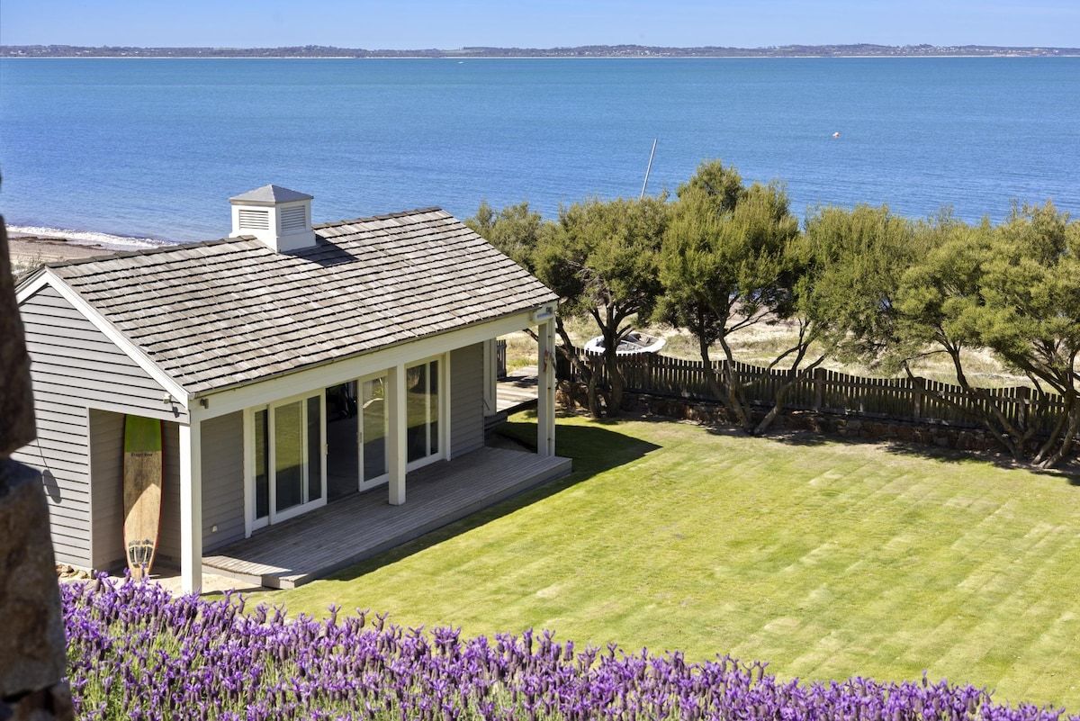 A coastal property with a house overlooking the sea, a well-maintained lawn, and a wooden fence.