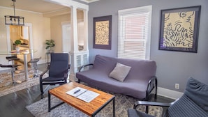 A living room with a gray sofa, a wooden coffee table, and a black chair. There are two framed artworks on the wall and a window with blinds. - Nice, Cozy and Comfortable 3 BR Near Downtown (San Antonio)