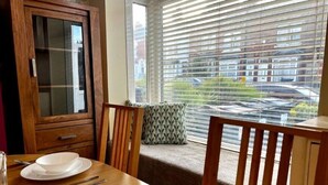 A dining area with a wooden table set for four, a cabinet, and a window with blinds. - Birmingham Cottage Contractors Family SelfCheck in (West Midlands)