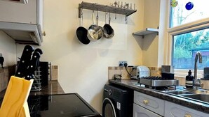 A compact kitchen with a washing machine, a built-in oven, and a window with a view of greenery. - Birmingham Cottage Contractors Family SelfCheck in (West Midlands)