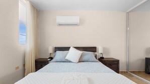 A bedroom with a bed, two bedside tables, a nightstand, a window with curtains, and an air conditioning unit on the wall. - Tropical Sunset Penthouse • Rooftop & Hot Tub (Cabo Rojo)
