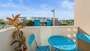 A balcony with a blue chair and table, a plant, and a building with a blue facade in the background. - Tropical Sunset Penthouse • Rooftop & Hot Tub (Cabo Rojo)