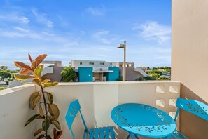 A balcony with a blue chair and table, a plant, and a building with a blue facade in the background. - Tropical Sunset Penthouse • Rooftop & Hot Tub (Cabo Rojo)