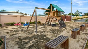 A playground with a wooden swing set, a slide, and a climbing structure. - Tropical Sunset Penthouse • Rooftop & Hot Tub (Cabo Rojo)