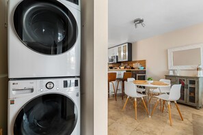 A laundry area with stacked washing machines and a modern kitchen with white cabinets, a dining table, and chairs. - Tropical Sunset Penthouse • Rooftop & Hot Tub (Cabo Rojo)