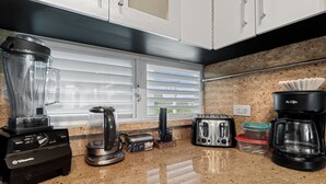 A kitchen with a Vitamix blender, a toaster, a coffee maker, and a window with blinds. - Tropical Sunset Penthouse • Rooftop & Hot Tub (Cabo Rojo)