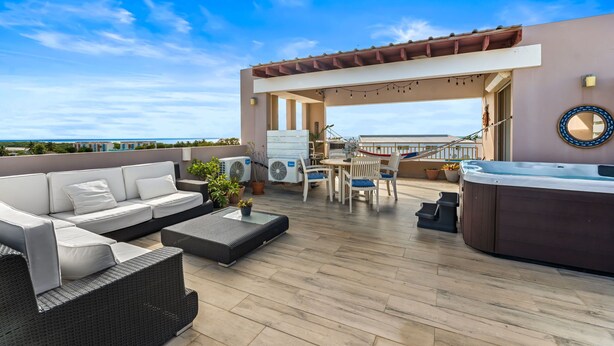 A rooftop terrace with a sofa, dining table, chairs, a hot tub, and outdoor air conditioning units. - Tropical Sunset Penthouse • Rooftop & Hot Tub (Cabo Rojo)