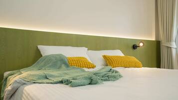 A neatly made bed with white and yellow pillows, a green blanket, and a wall-mounted light fixture.