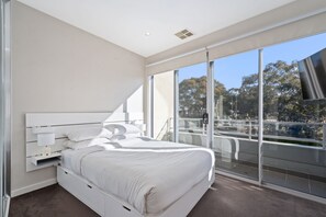 A modern bedroom with a large bed, built-in bedside tables, and a view of a cityscape through floor-to-ceiling windows. - Stylish Curtin Stay With Balcony Views (Canberra)