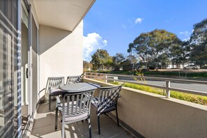 A balcony with two chairs and a table, overlooking a road and trees. - Stylish Curtin Stay With Balcony Views (Canberra)