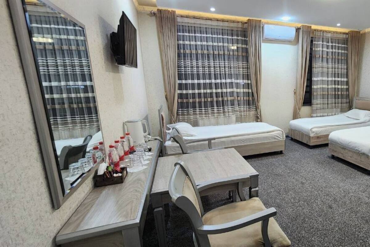 A hotel room with four single beds, a desk with a chair, a small table, and a TV mounted on the wall.
