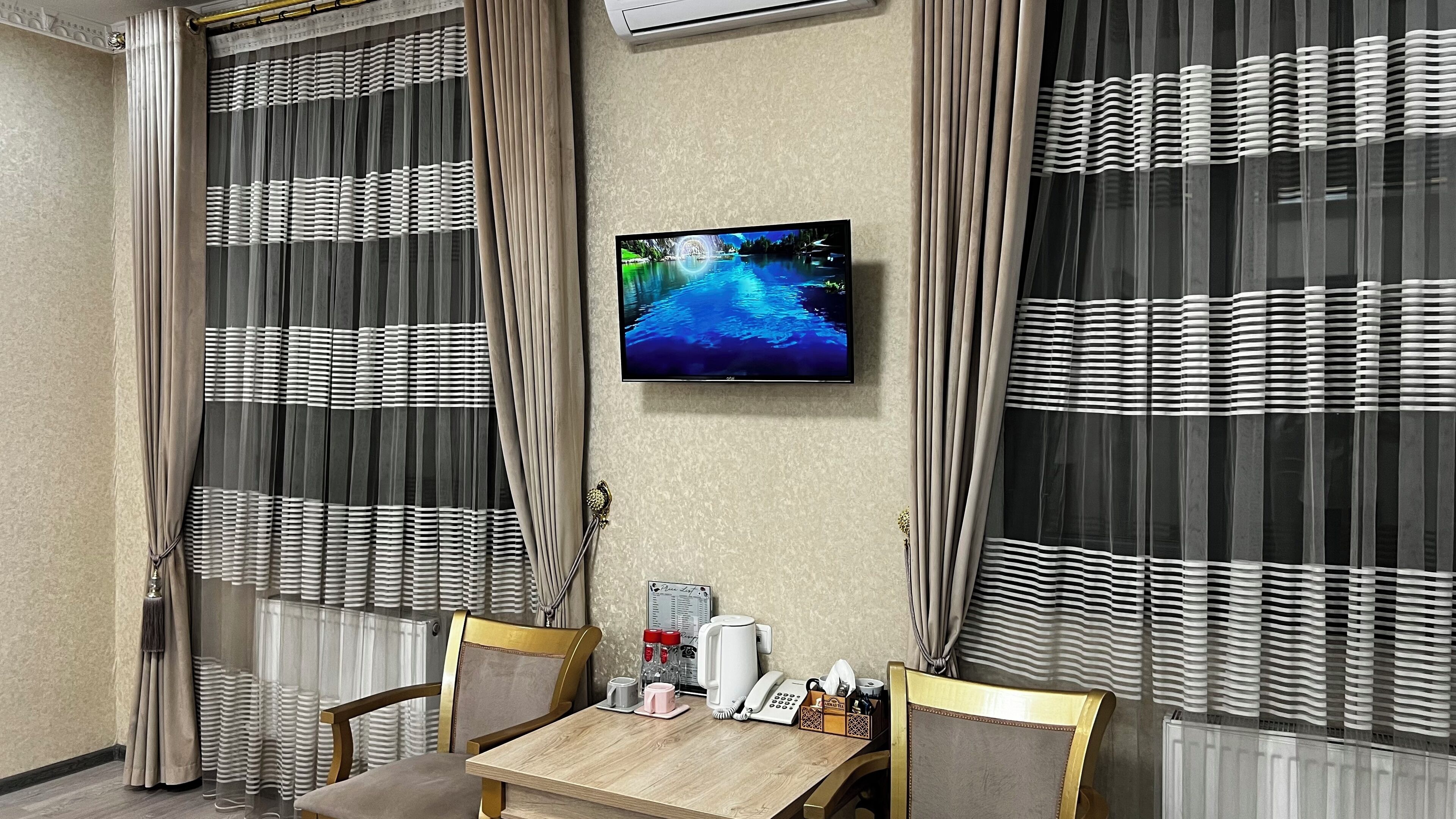 Habitación de hotel con una mesa de madera, dos sillas, un televisor montado en la pared y cortinas con estampado a rayas.