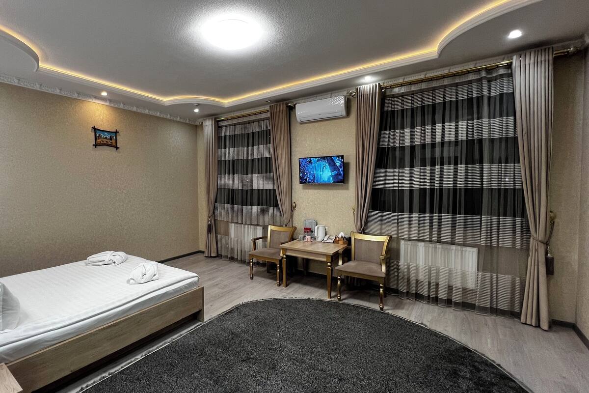 A hotel room with a bed, a desk, a chair, a TV, and curtains.