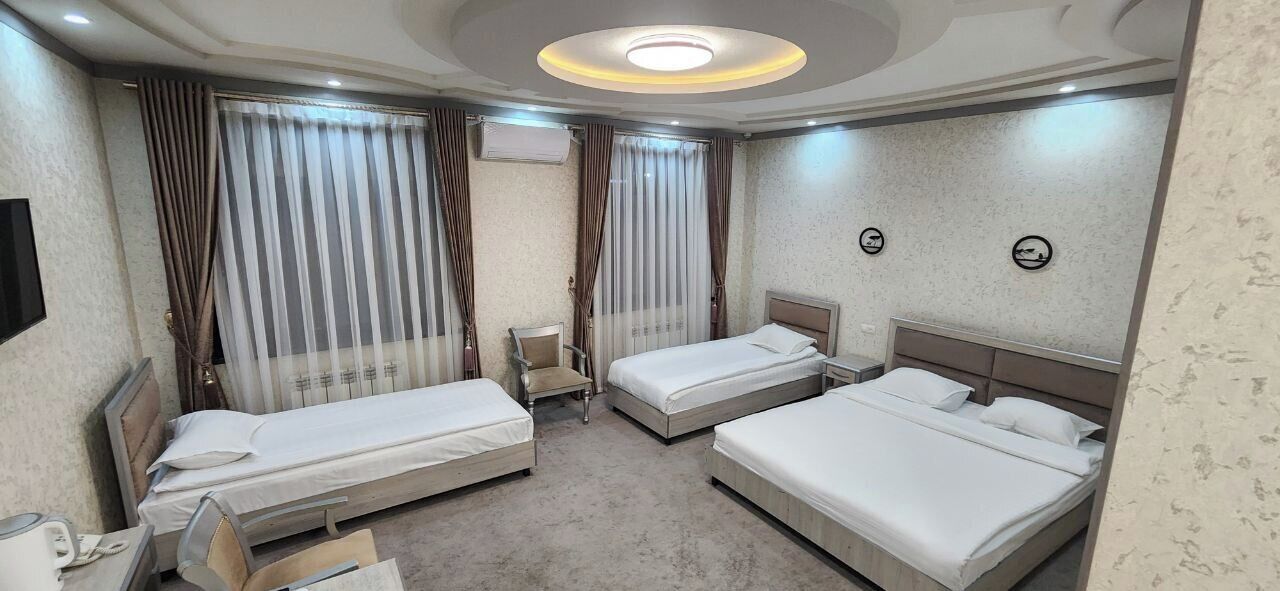 A hotel room with two single beds, a chair, a small table, and a television.